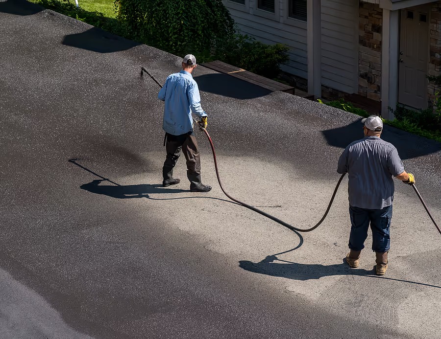 Aerial view of two crew members hand-applying sealcoat to a residential driveway in front of a home
